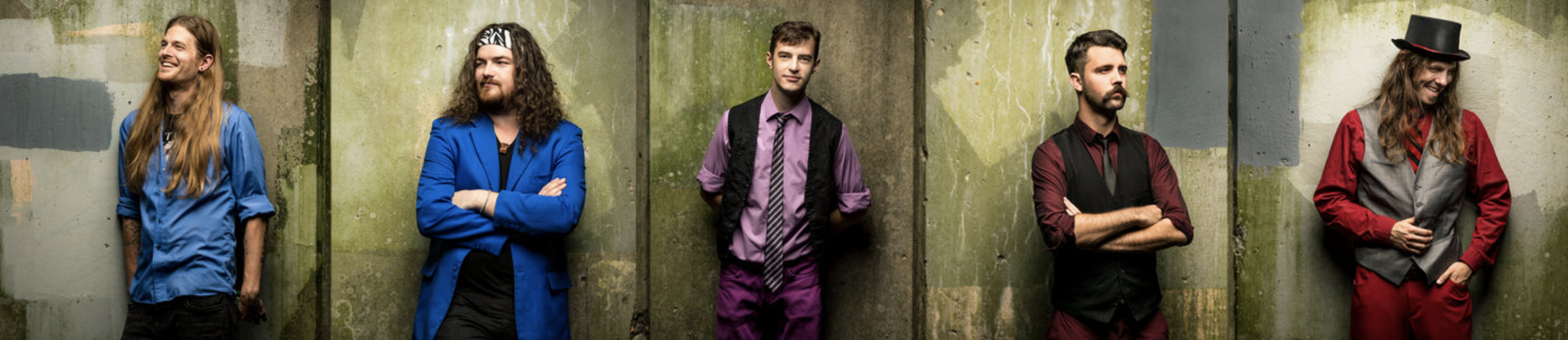 a group of male band members pose differently against a concrete wall while wearing different colored clothing to demonstrate one of the tips for great branding photos